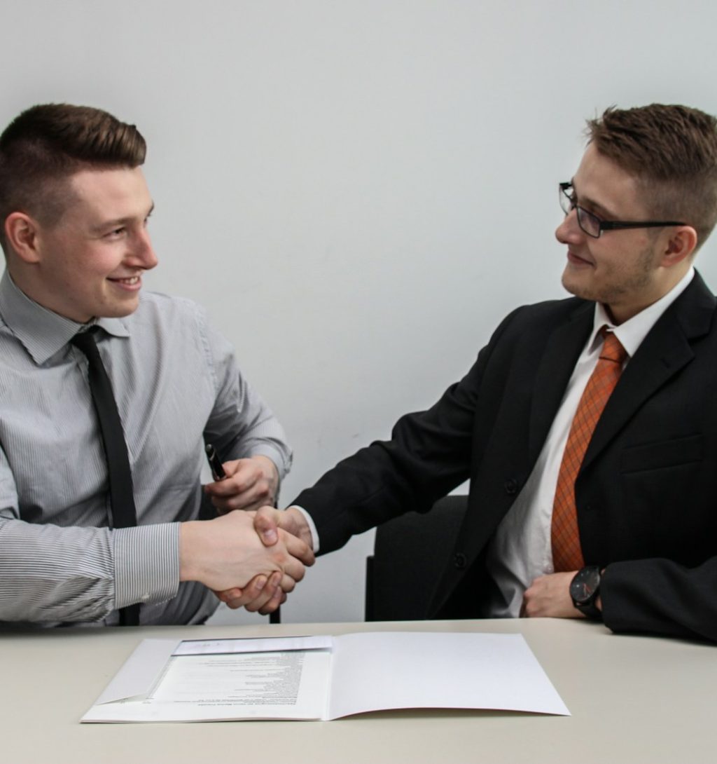 two men facing each other while shake hands and smiling